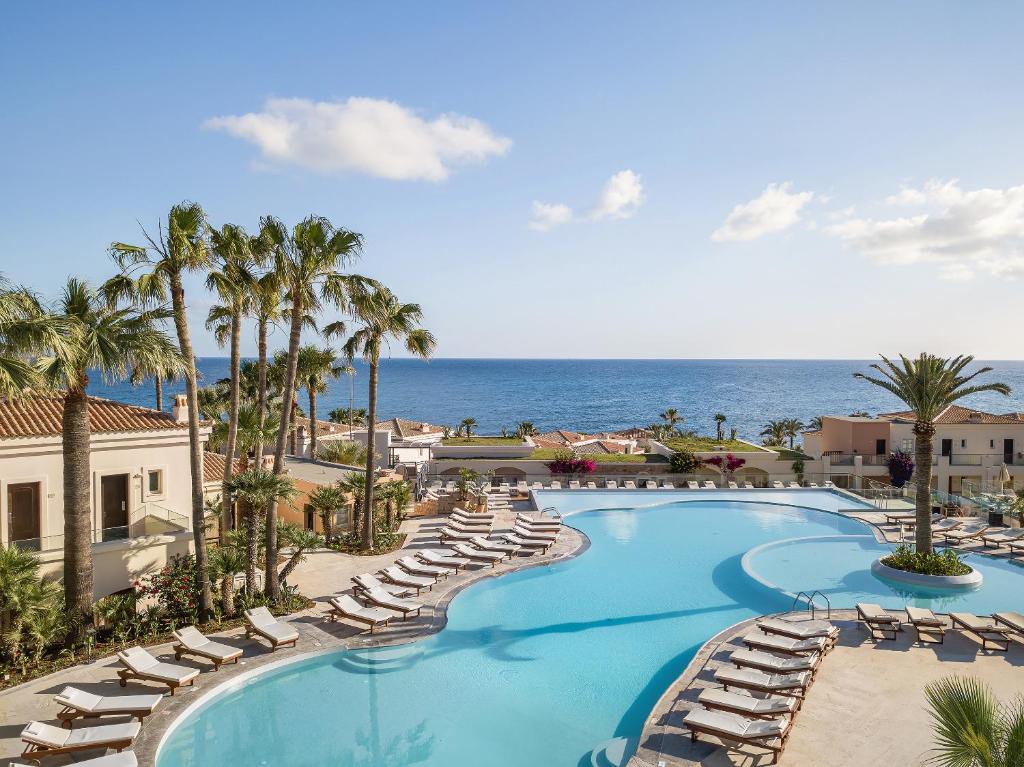 an image of a swimming pool with lounge chairs and the ocean at Grecotel Marine Palace & Aqua Park in Panormos Rethymno