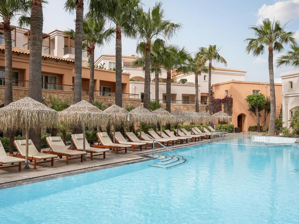 a pool with chairs and umbrellas and palm trees at Grecotel Marine Palace & Aqua Park in Panormos Rethymno