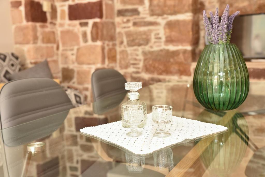 a glass table with a green vase and glasses on it at Kentos Charming Stone Escape Near Fishing Harbor in Katarráktis