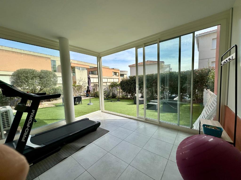 une salle de sport avec un tapis de course et une grande fenêtre dans l'établissement Appartement Cardellina Jardin & Ville, à Calvi