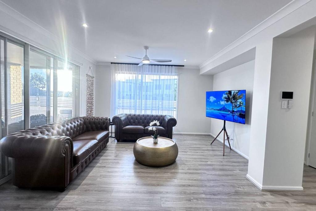 Lotus Grand Home in Mango Hill Sleeps 8 في البحيرات الشمالية: غرفة معيشة مع كنبتين جلديتين وتلفزيون