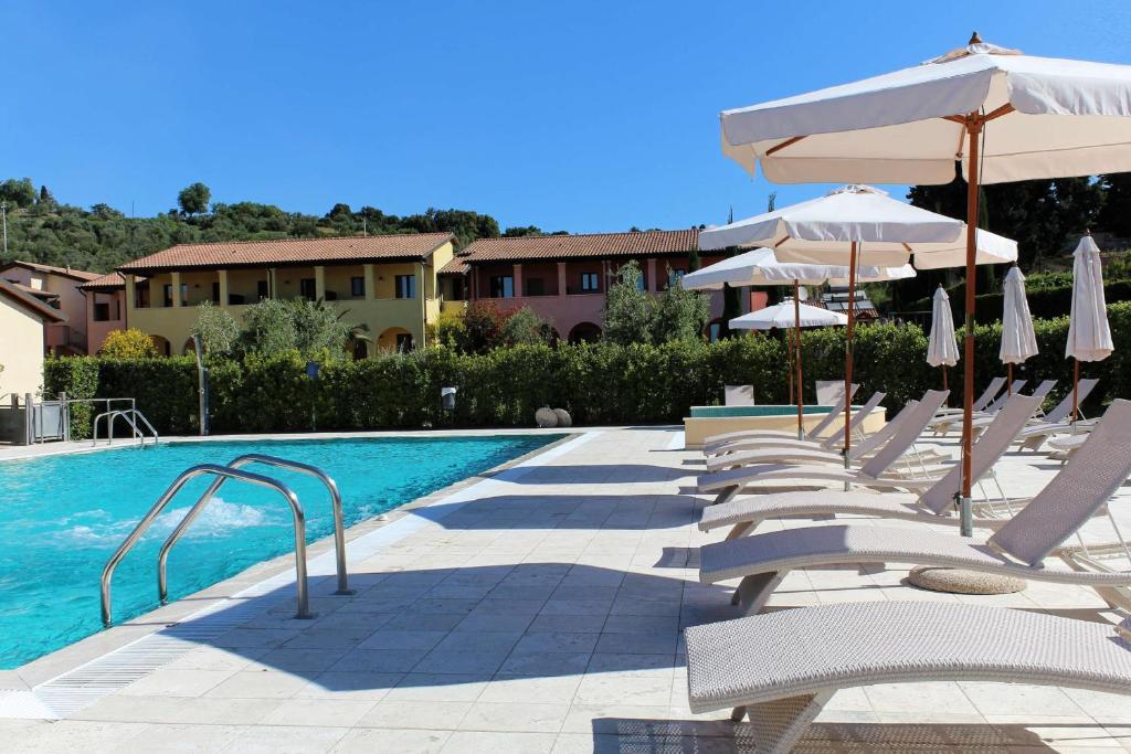 un gruppo di sedie e ombrelloni accanto alla piscina di Le Corti Del Sole Residence a Venturina Terme