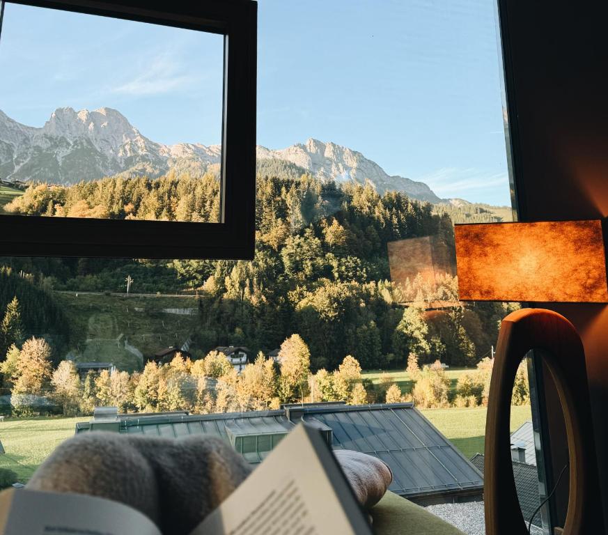 a person reading a book in front of a window at Hotel Der Löwe LEBE FREI in Leogang