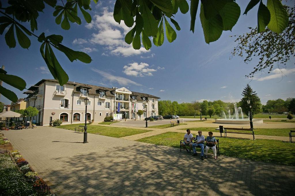 drie mensen op een bankje voor een gebouw bij Xavin Wellness Hotel & Restaurant in Harkány