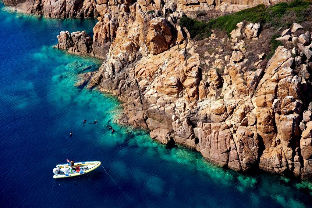 a boat in the water next to a rocky cliff at Chia Laguna - Hotel Village in Chia