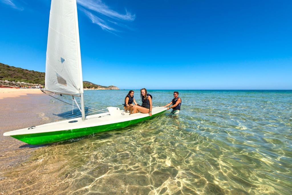 three people sitting on a sail boat on the beach at Chia Laguna - Hotel Village in Chia