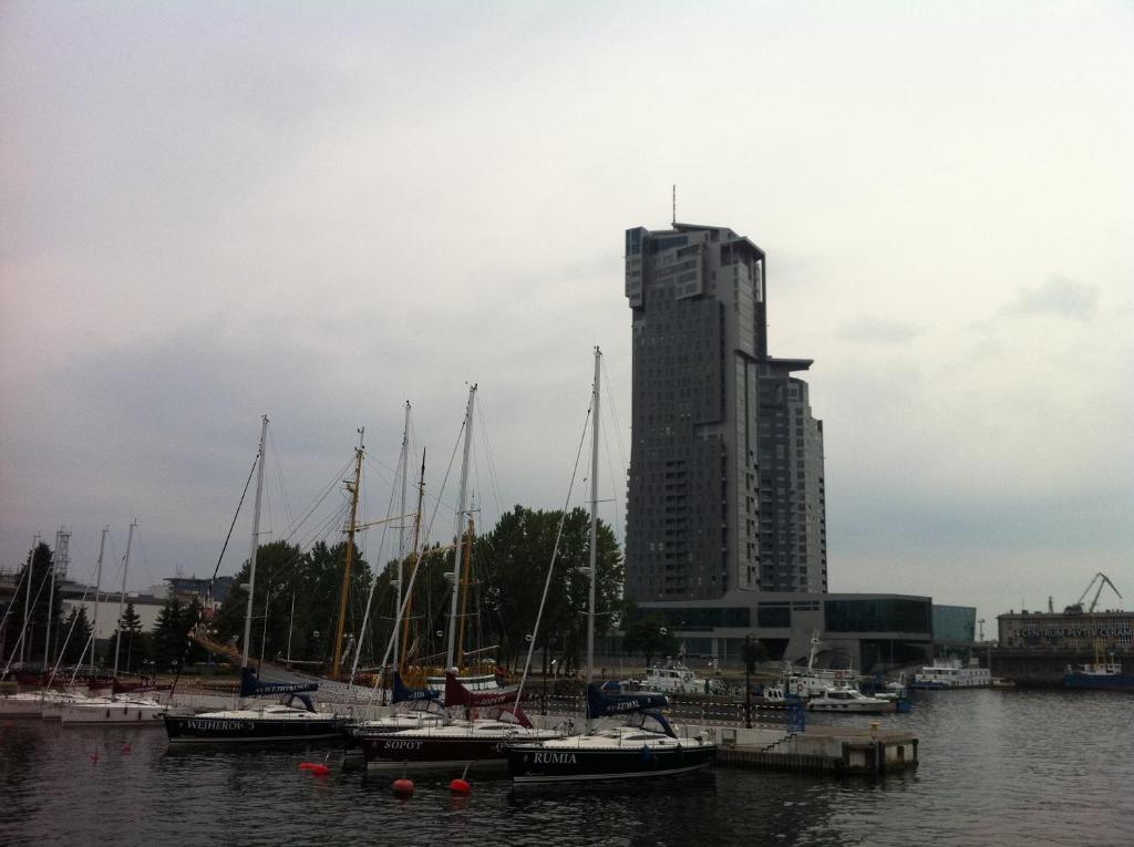 a group of boats docked in a harbor with a tall building at Sea Towers in Gdynia