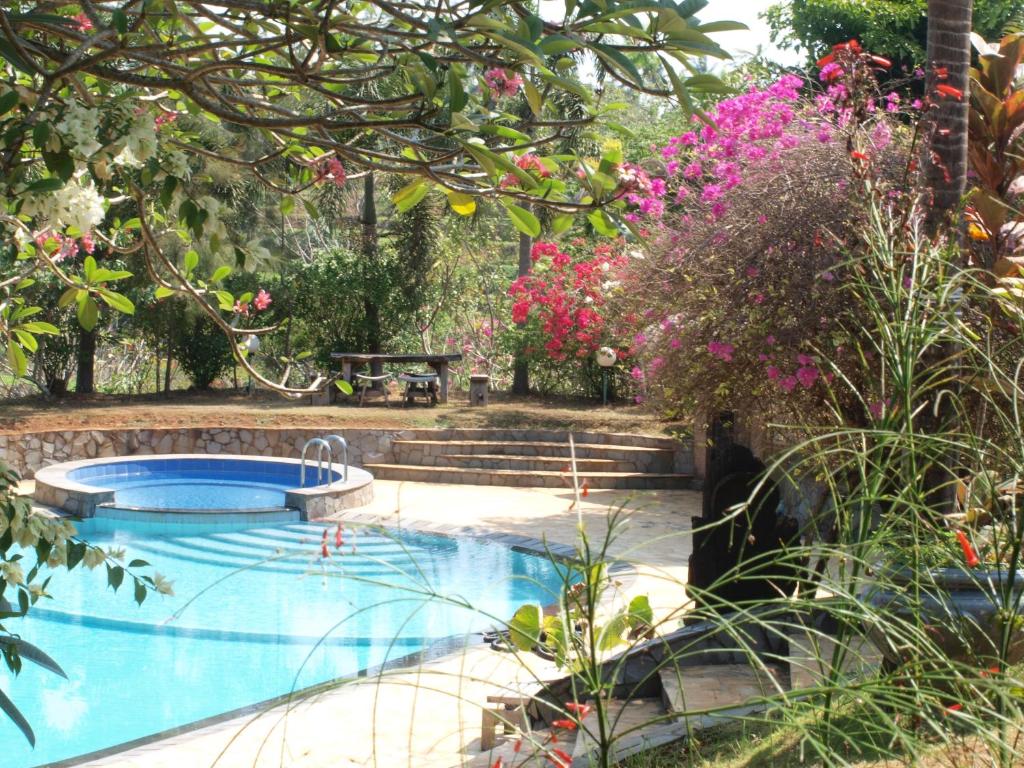 a swimming pool in a garden with pink flowers at The Gecho Inn Country in Jepara