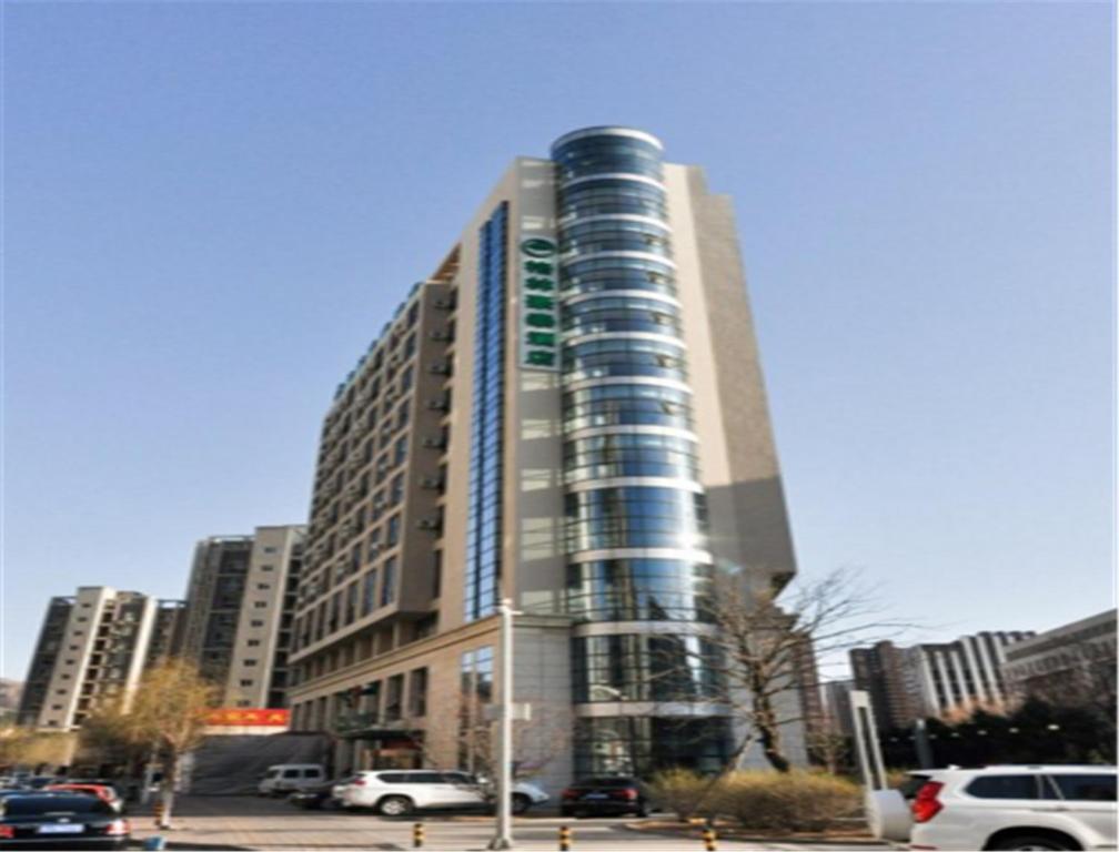a tall building with cars parked in a parking lot at GreenTree Inn HeBei ChengDe Railway Station Southeast ChengDe Century City Business Hotel in Chengde