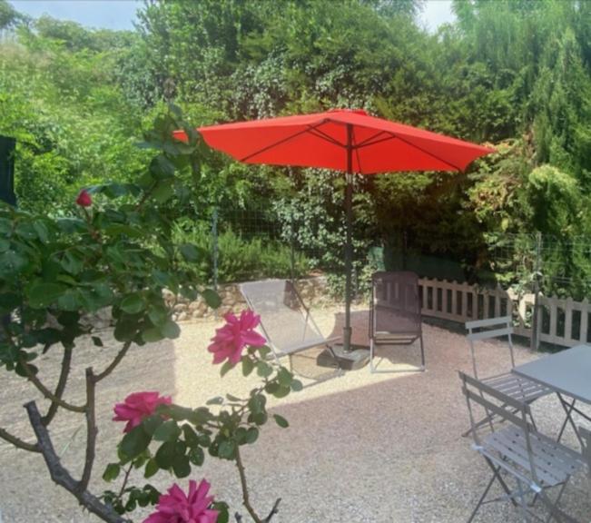 un parapluie rouge, deux chaises et une table avec des fleurs roses dans l'établissement BEAUSOLEIL , appartement neuf, climatisé , Jardin clos , 2 chambres, parking privé, calme, 900 m du centre de nyons, à Nyons