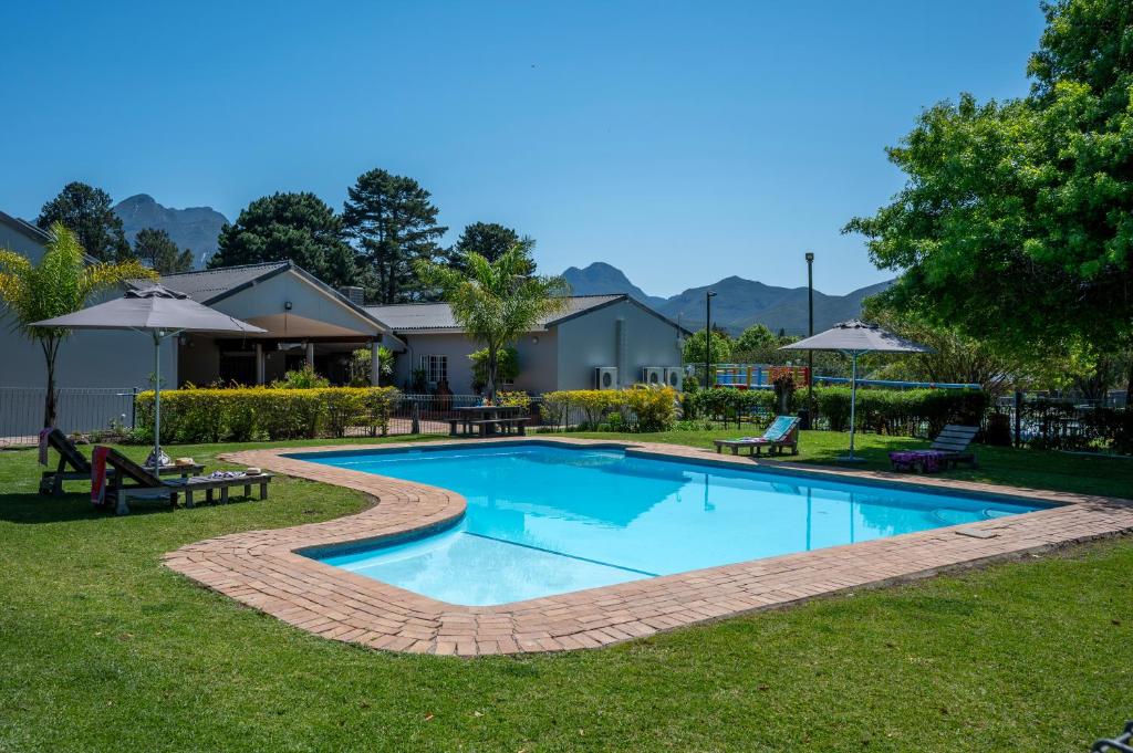 - une piscine dans une cour avec des bancs et des parasols dans l'établissement Pine Lodge George, à George