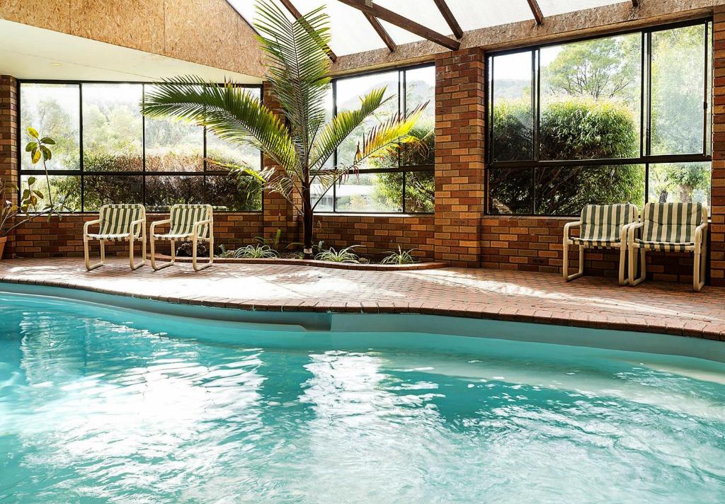 a swimming pool with two chairs and a group of windows at Pinnacle Holiday Lodge in Halls Gap