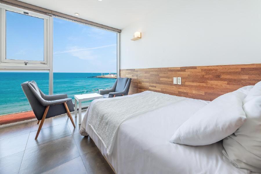 a bedroom with a bed and two chairs and a large window at Jeju Dalbeach Pension in Jeju