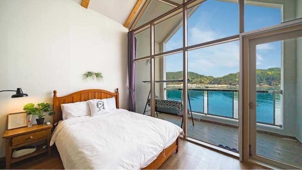 a bedroom with a bed and a large window at Tongyeong Maremio Oceanview Pension in Tongyeong