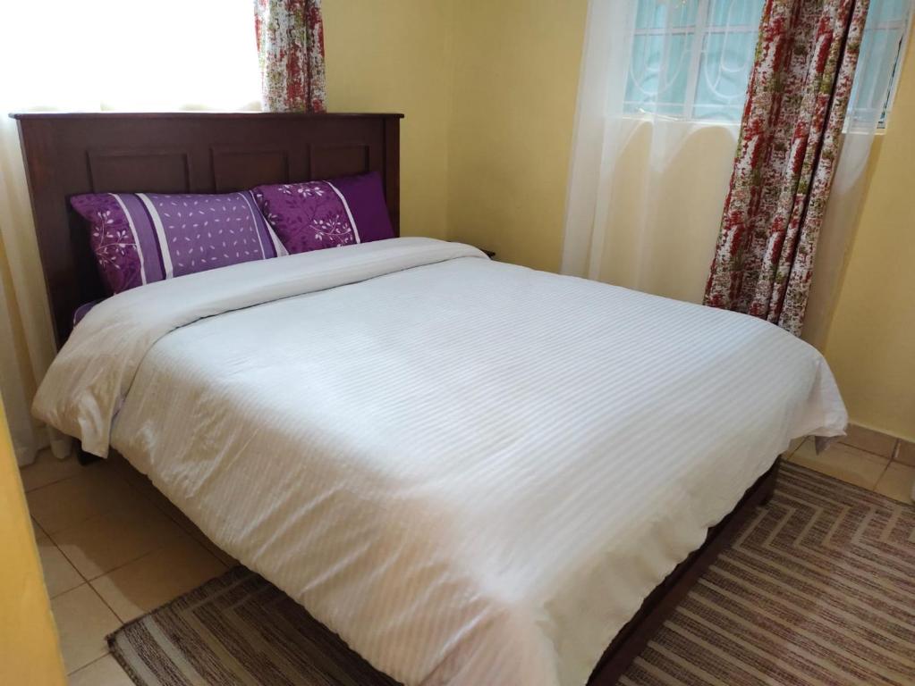 a bed with white sheets and purple pillows next to a window at Zoe Homes Kericho in Kericho