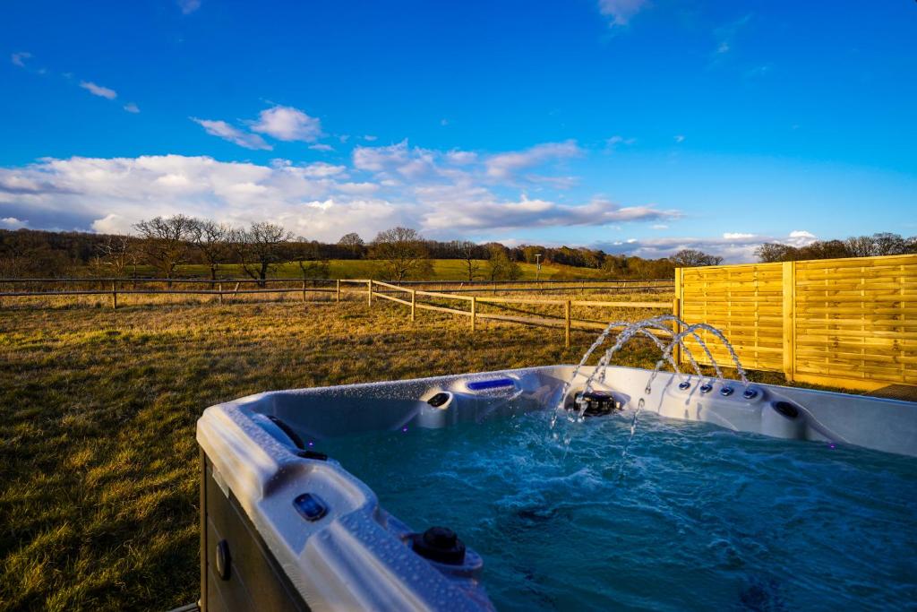 a hot tub in a field next to a fence at Starlight Lodge - 4BR Luxury Barn with Hot Tub in Tandridge