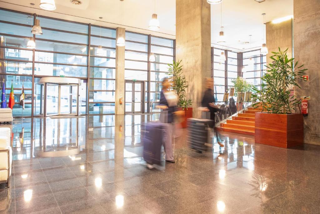 A spacious glazed lobby has polished stone floors, plants and a prominent staircase.