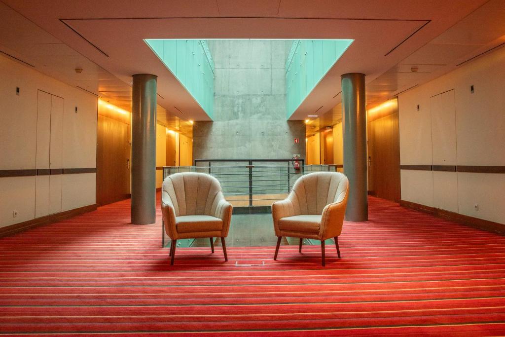 Two armchairs sit in a bright hotel corridor beside an interior atrium.