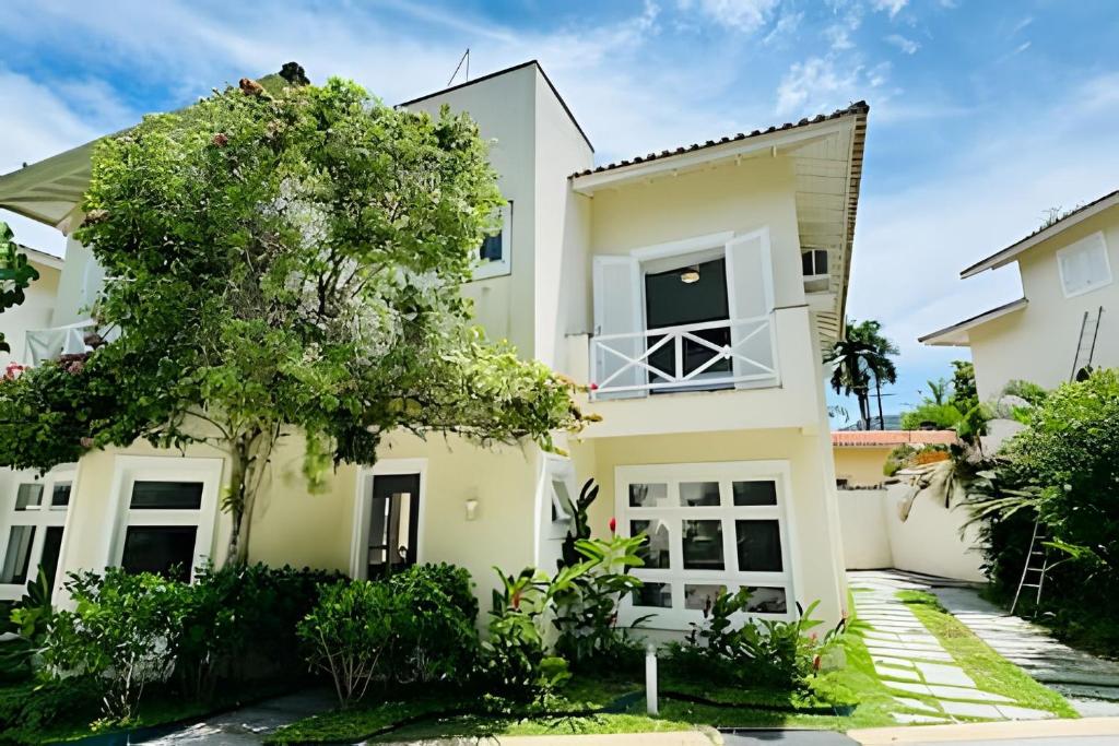 a white house with a tree in front of it at Casa de condomínio em Juquehy - SP (4) in Praia de Juquehy