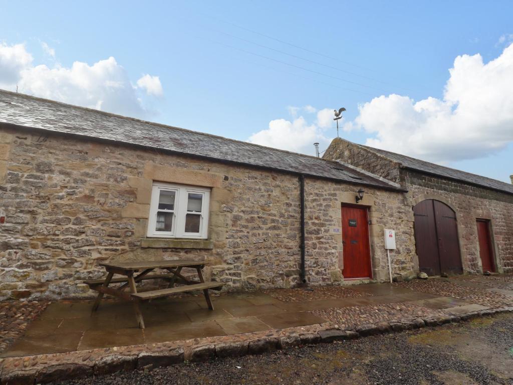 a picnic table outside of a stone building with a red door at Christon Well Cottage in Alnwick