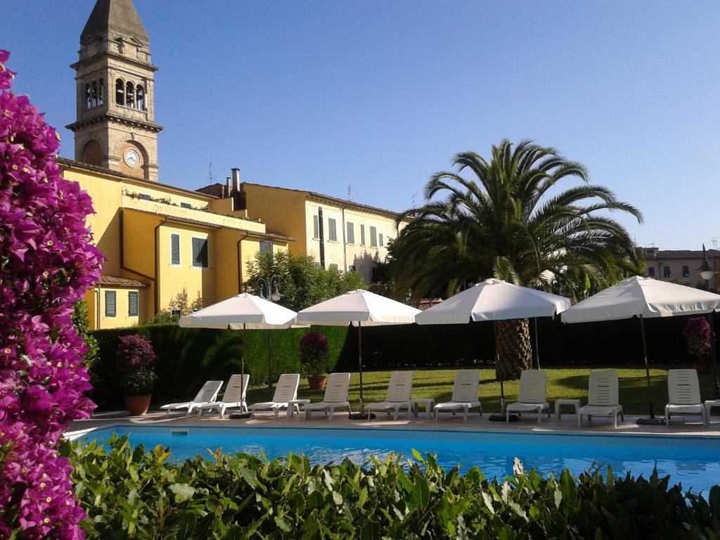 a pool with chairs and a building with a clock tower at Albergo Roma in Casciana Terme