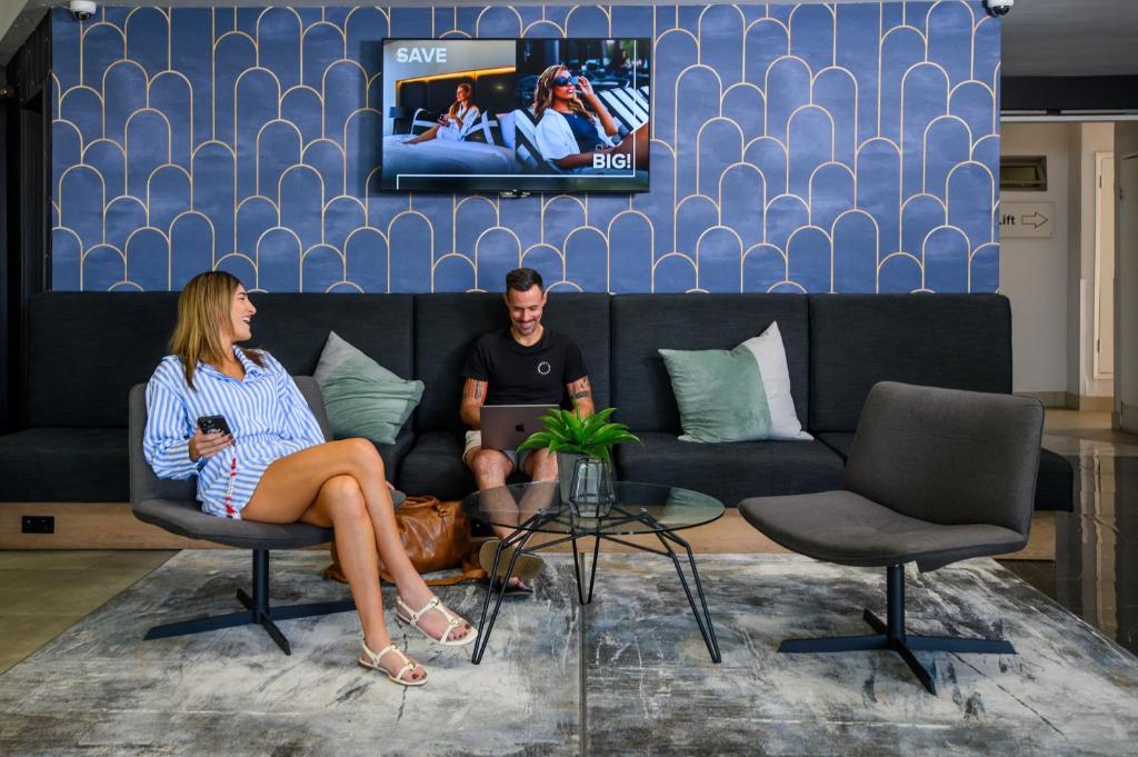 a man and woman sitting on a couch watching tv at The Capital on Bath in Johannesburg