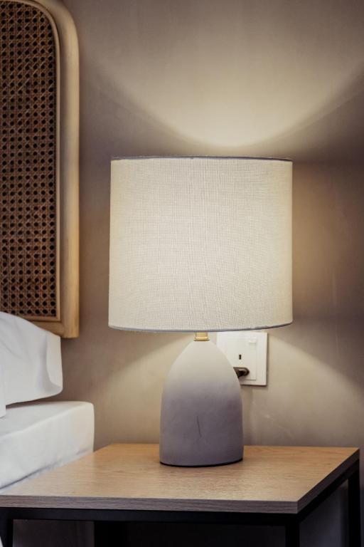 A bedside table with a lamp, power outlet and woven rattan bedhead beside it.
