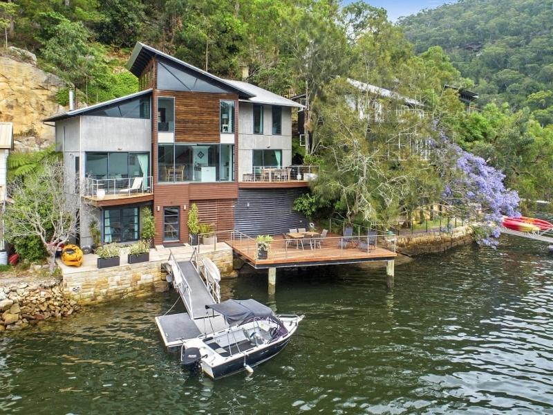 una casa su un molo con una barca in acqua di Berowra Waters Glass House a Berrilee