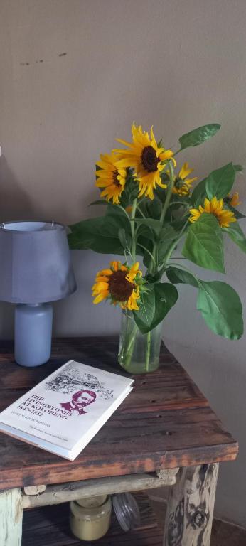 a vase of sunflowers on a table with a book at Kolobeng Cottages in Gaborone