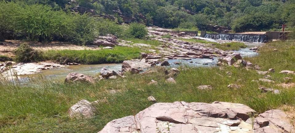 a river with some rocks and grass and a field at Kolobeng Cottages in Gaborone