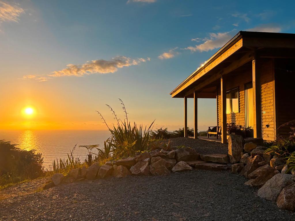 a house on the beach with the sunset in the background at Pahautane Ridge - Elevated Sea Views Outdoor Stone Bath in Punakaiki