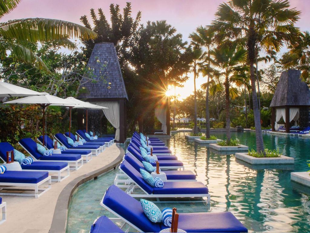 a pool with blue lounge chairs and palm trees at Sofitel Bali Nusa Dua Beach Resort in Nusa Dua