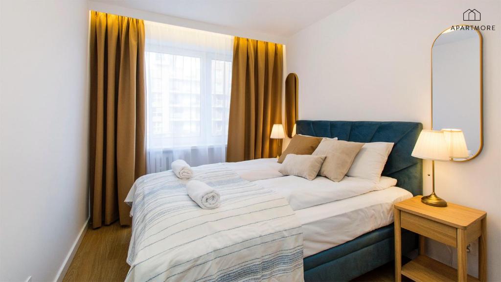 Sunlit bedroom with teal upholstered bed, striped bedding, gold curtains and bedside table lamp