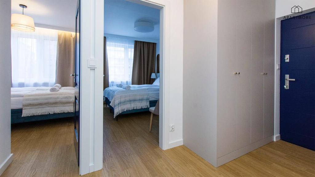 Hallway with open doors revealing two beds in adjoining bedrooms, wooden floor and blue entrance door.