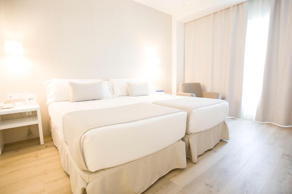 a white bedroom with two beds and a desk at Hotel Albufera in Alfafar