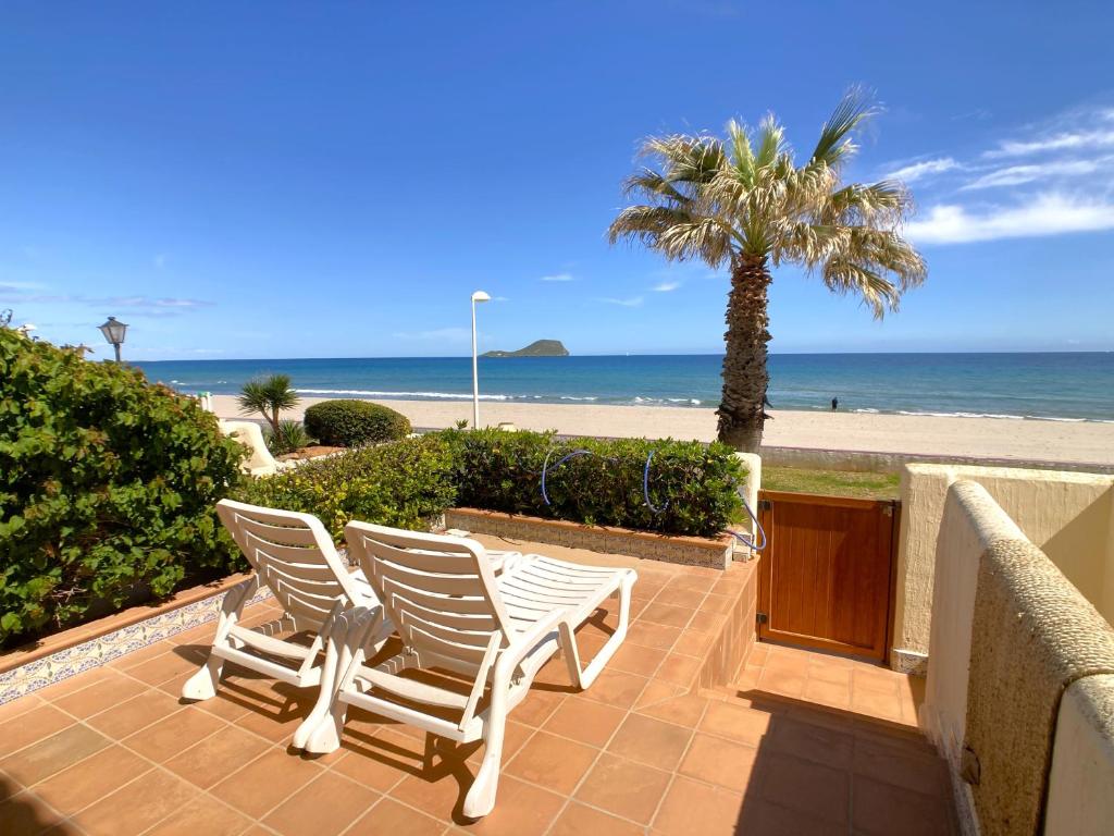 two chairs and a palm tree on a patio with the beach at Spanish Connection - Villa Morena in La Manga del Mar Menor