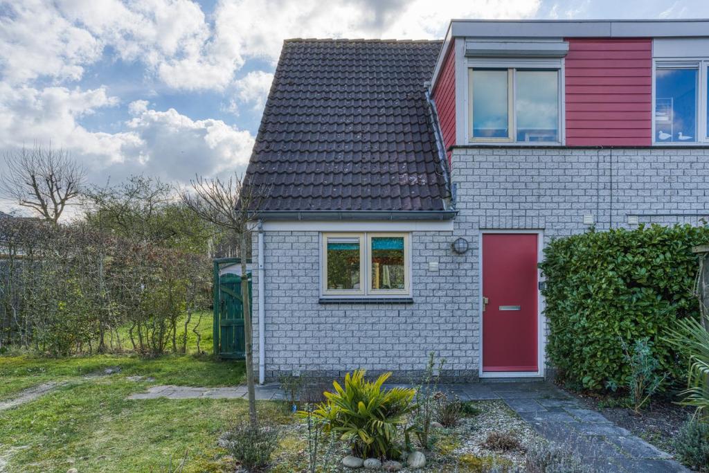 a small white house with a red door at Vakantiehuis, Villapark Oesterbaai 39, aan zee, grenzend aan speeltuin in Wemeldinge