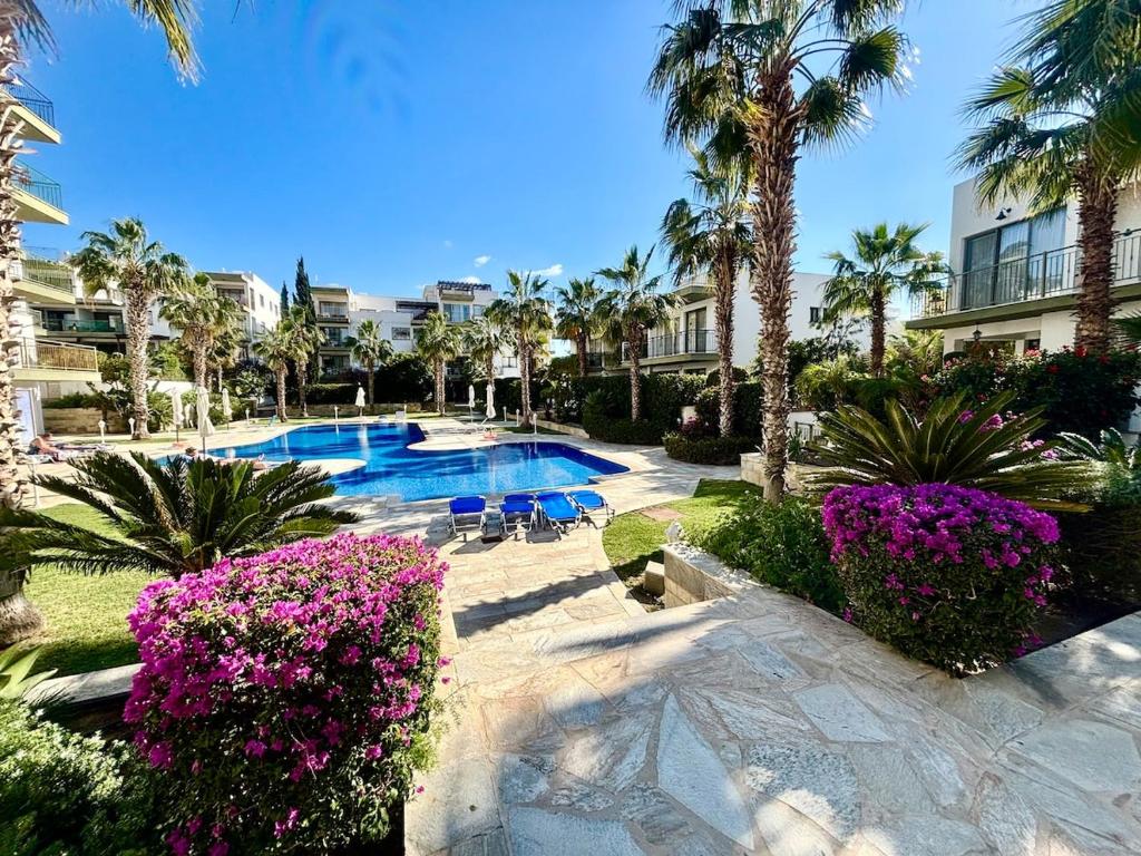 a resort swimming pool with palm trees and purple flowers at Beautiful house near Venus beach in Paphos City