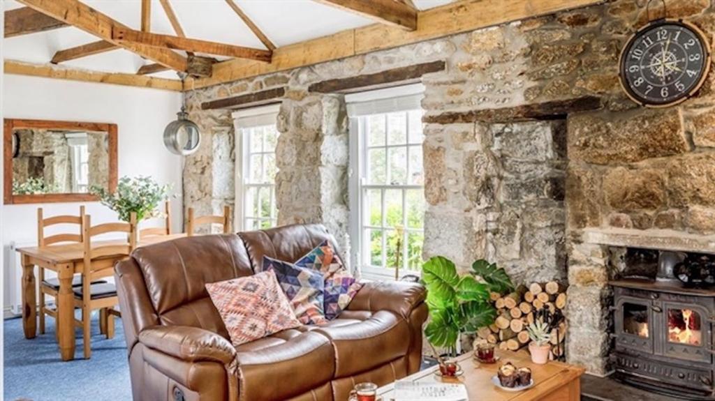 a living room with a leather couch and a stone wall at Boatsman's Cottage- sleeps 4- Garage- Mousehole in Mousehole
