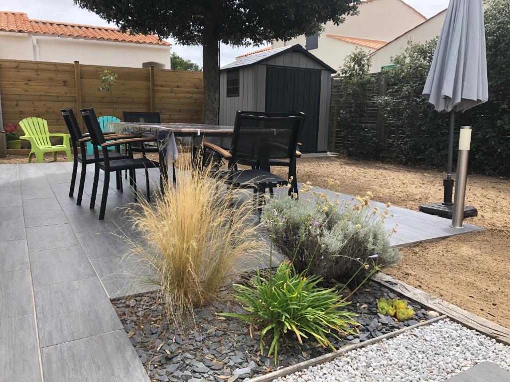 un patio avec une table, des chaises et un parasol dans l'établissement Maison en bord de mer et lisière de forêt, à La Tranche-sur-Mer