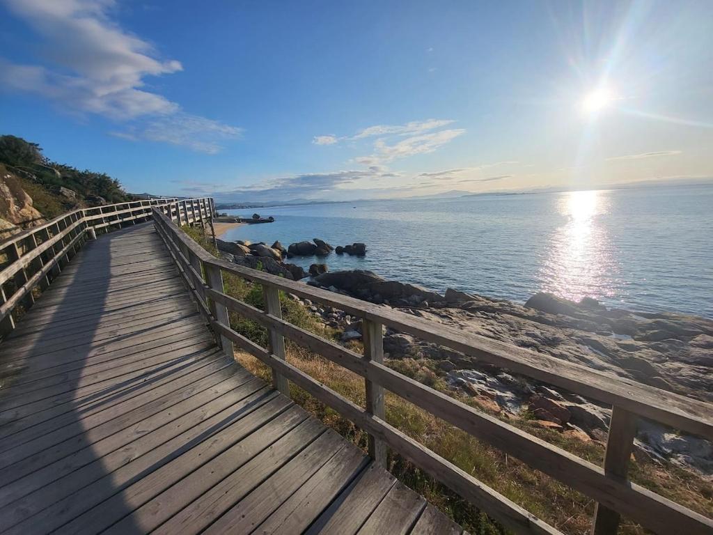 a wooden boardwalk next to the ocean with the sun shining at Casa con vistas al mar, playa 300 m, parking, wifi in Ribeira