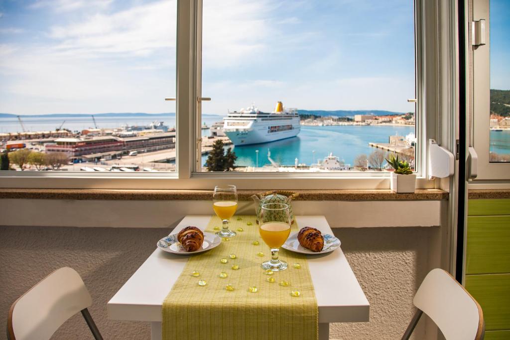 Apartment Amazing View في سبليت: طاولة مع كأسين من النبيذ وسفينة بحرية في نافذة