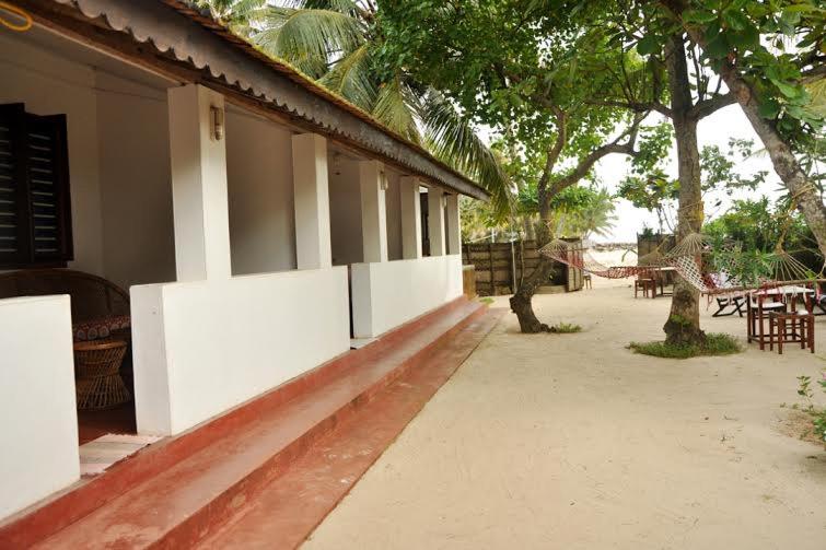 a walkway next to a building with tables and trees at Angeo Beach House in Alleppey