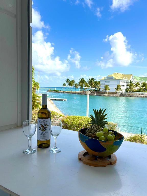 a bottle of wine and two glasses and a bowl of fruit at Bleu Lagon - Vue mer, Piscine, Marina et Golf in Saint-François