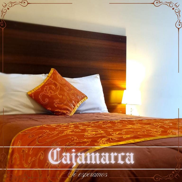 a bed with an orange comforter and white pillows at Hotel Los Nogales in Cajamarca