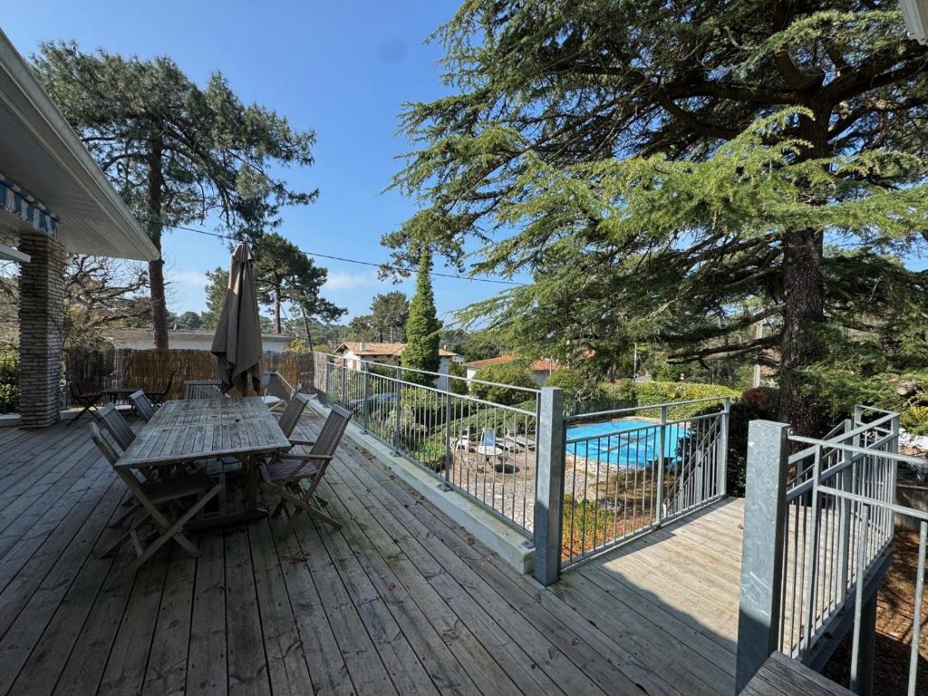 une terrasse en bois avec une table, des chaises et un parasol dans l'établissement Maison rénovée avec piscine aux Abatilles, Arcachon - FR-1-474-274, à Arcachon