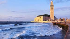 un bâtiment avec une tour d'horloge à côté de l'océan dans l'établissement marjana room, à Casablanca