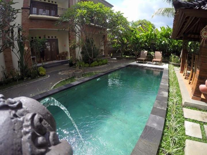 a swimming pool with a fountain in front of a house at Nami House in Ubud