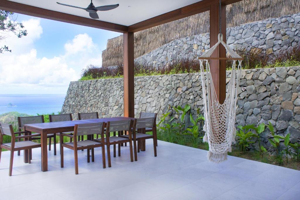 a patio with a table and chairs and a stone wall at Selong Selo Resort and Residences in Selong Belanak