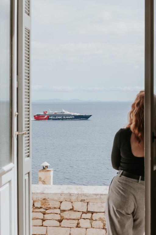 a woman looking out a window at a ship in the water at The Hub Syros in Ermoupoli